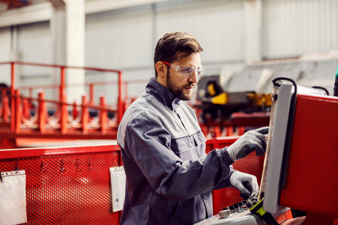A heavy industry worker controls the machine and looks at the display while standing in the facility.
